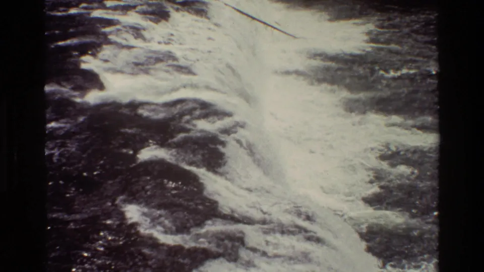 Grand Teton waterfall footage frame with bright foaming water and dark rock texture in a handheld 8mm view.