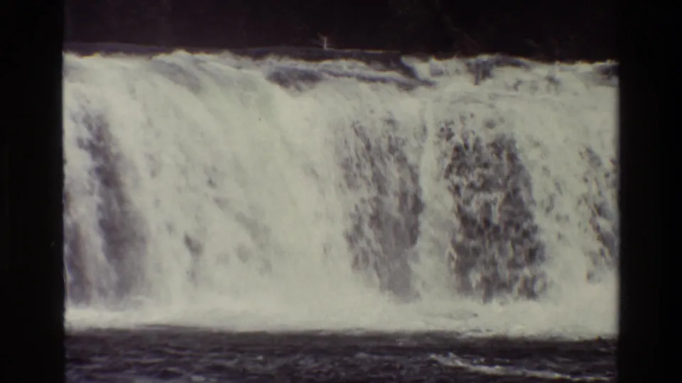 1980 Grand Teton frame shows a waterfall flowing into a broad river, with white foam and dark water visible at the base.