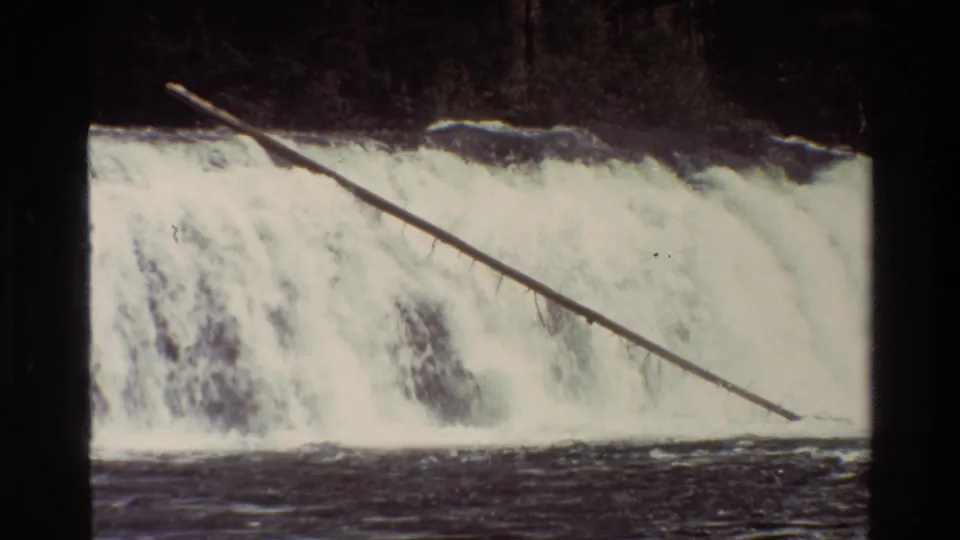 Archival 8mm Grand Teton footage showing foaming white water and a fallen tree trunk stretching across the waterfall.