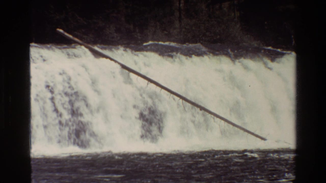 1980 Grand Teton home-movie frame of a wide cascade, dark river water, and a long log slanting across the falls.