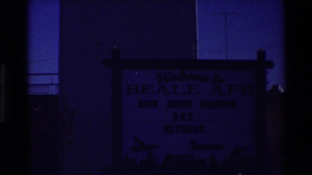 Dim view of a Beale AFB welcome sign beside a tall pale building wall.