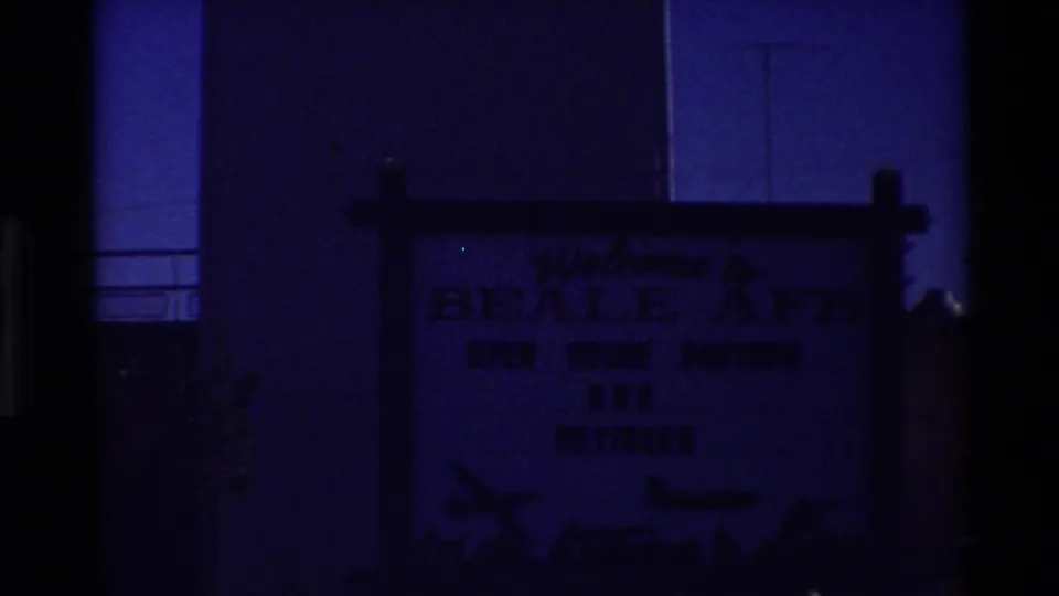 Dark blue 8mm view of a welcome sign for Beale AFB open-house visitors near the base tower structure.