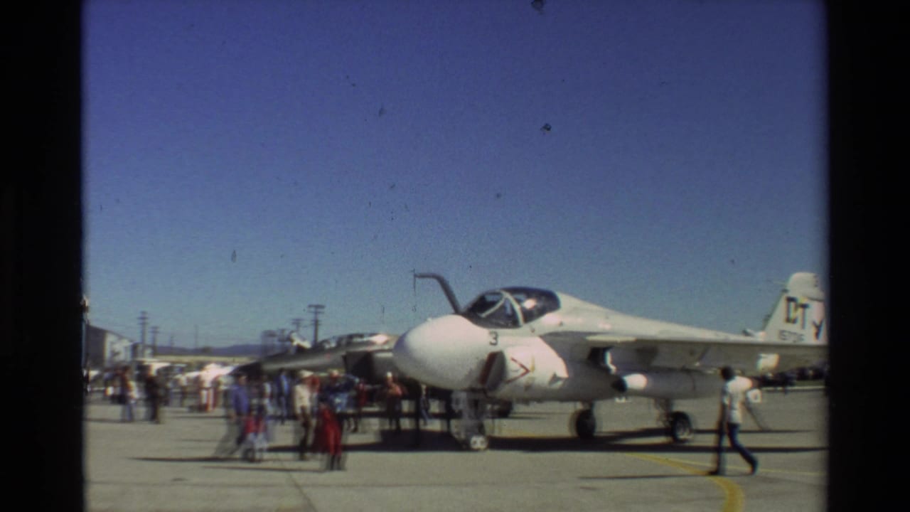 White A-7 jet on a tarmac with civilians gathered around it.
