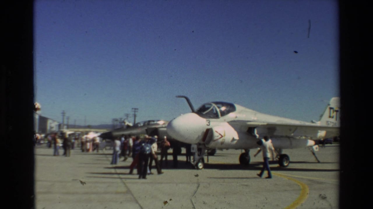 Visitors on the Beale AFB tarmac stand near the nose and wing of a white A-7 Corsair II in 1981 footage.