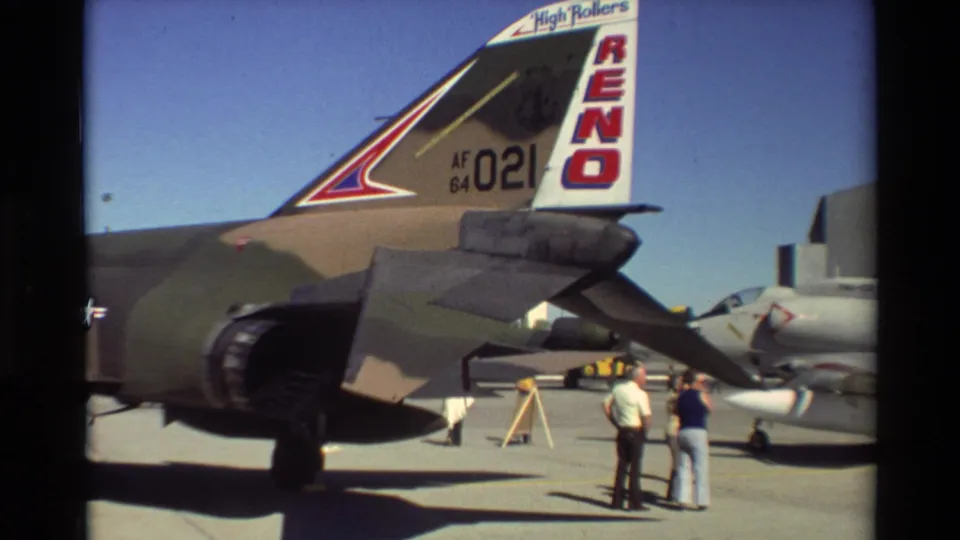 A camouflaged F-4 Phantom II tail with RENO markings is shown on the Beale AFB tarmac as visitors look on.