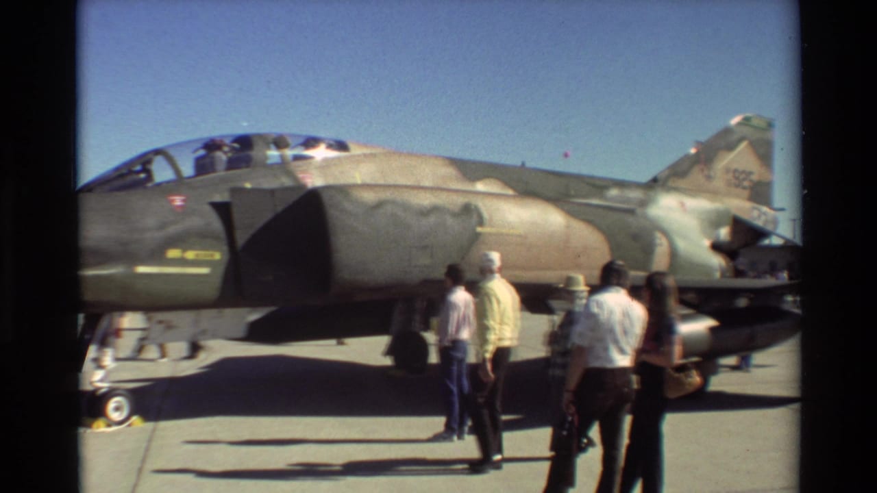 Adults walk alongside the displayed military jet, with the tail and cockpit visible.