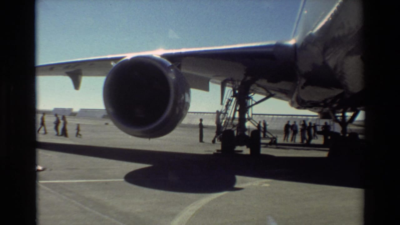 1981 Beale AFB frame showing the underside of a U.S. Air Force aircraft wing, a large turbofan engine, mobile stairs, and people nearby.