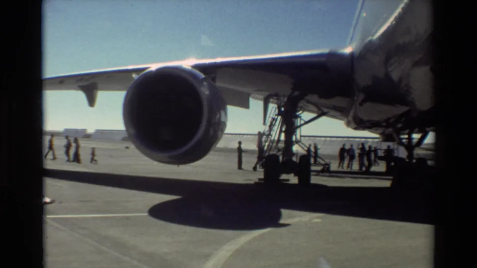 1981 Beale AFB frame showing the underside of a U.S. Air Force aircraft wing, a large turbofan engine, mobile stairs, and people nearby.