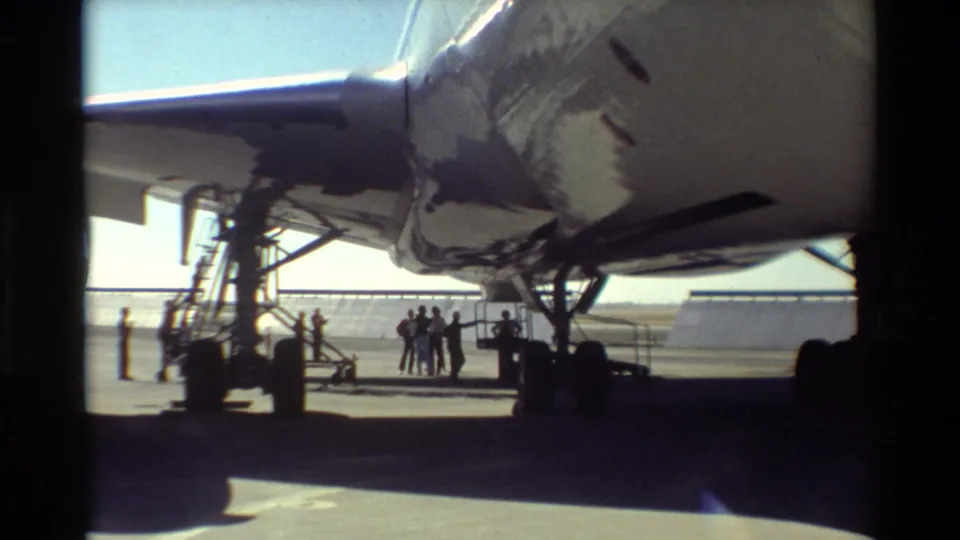 1981 Beale AFB frame showing the underside of the U.S. Air Force aircraft, mobile stairs, landing gear, and people gathered in sunlight.