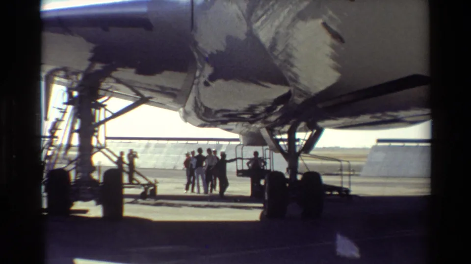 At Beale AFB in 1981, silhouetted people stand beneath a large aircraft wing on a sunlit tarmac.