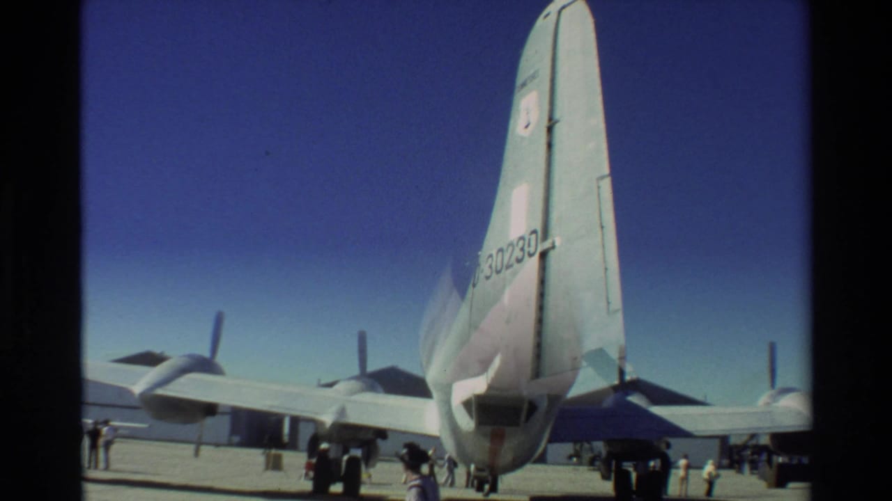 Rear view of a large USAF aircraft on a tarmac with people near the landing gear.