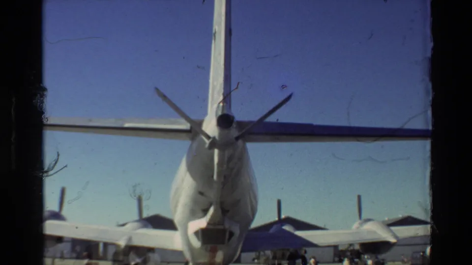 Handheld 8mm frame from Beale AFB showing a close rear view of a USAF aircraft tail, wing, propellers, and surrounding tarmac activity.
