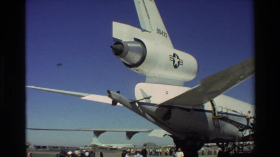 1981 Beale AFB frame showing a USAF-marked aircraft tail section, wing, service stairs, and distant people on the tarmac.