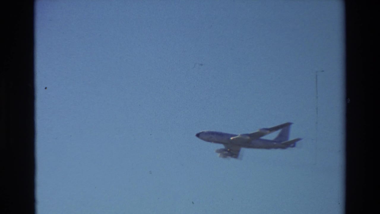 Distant four-engine tanker aircraft flying across a clear blue sky.