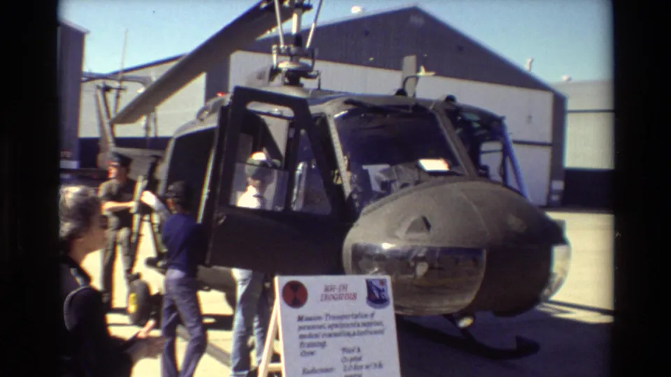 Closer 1981 Beale AFB view of a military helicopter on display, with people beside the cockpit and a sign in front of the aircraft.