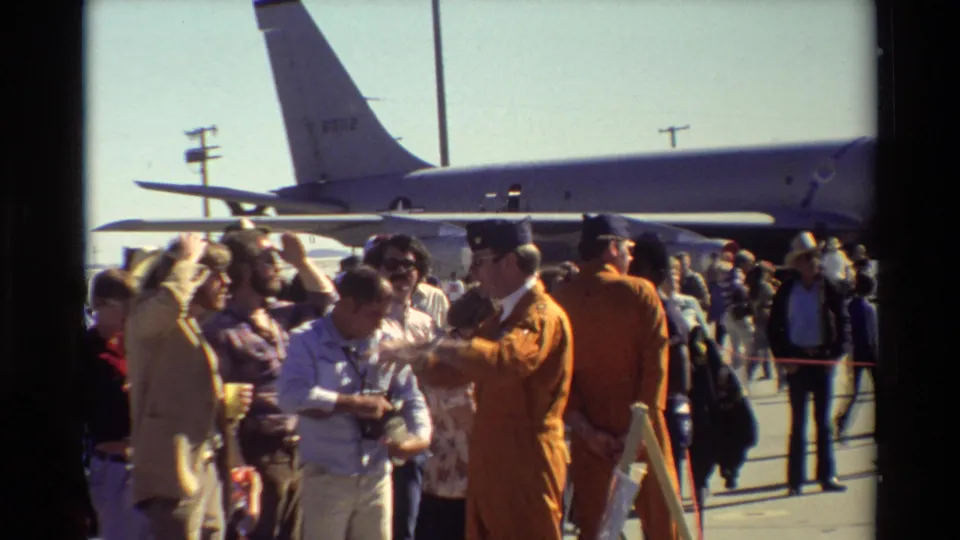 Civilians and personnel mingle near a large aircraft at Beale AFB, including a visible orange flight suit in the foreground.