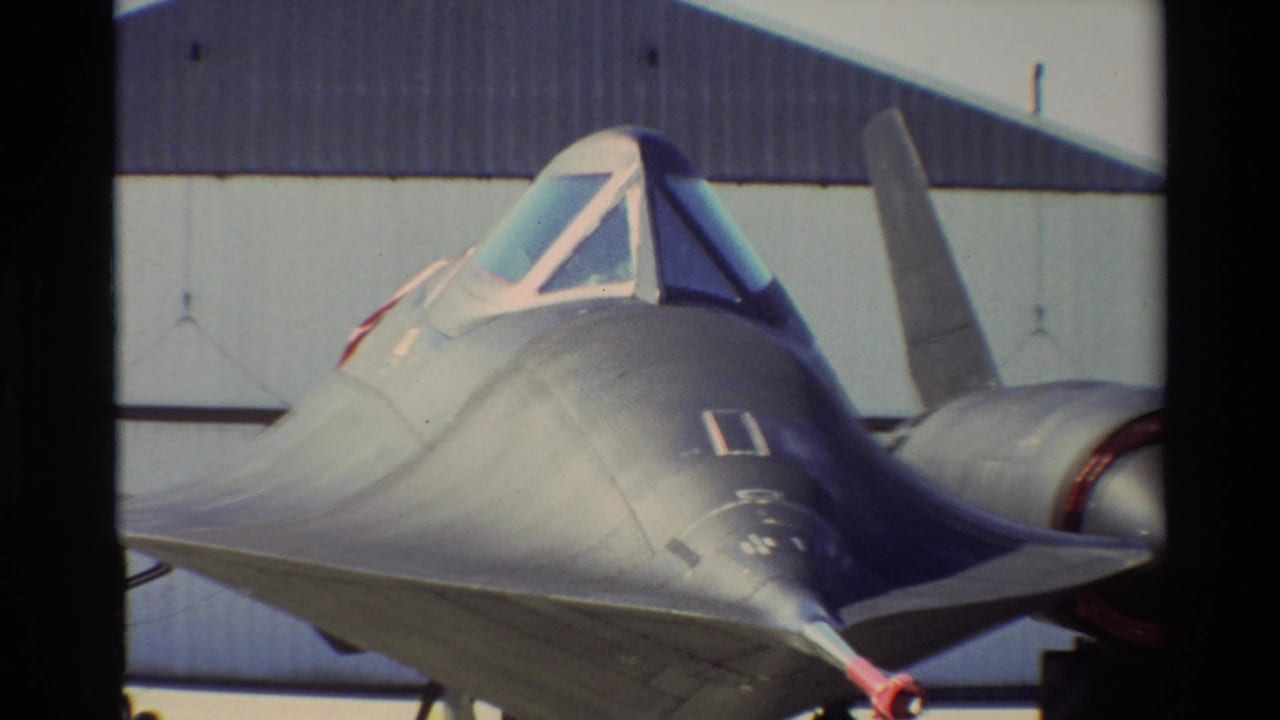 1981 Beale AFB 8mm frame showing the SR-71 Blackbird from a close front-quarter angle, with cockpit canopy, nose, and hangar behind it.