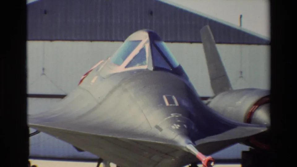 1981 Beale AFB 8mm frame showing the SR-71 Blackbird from a close front-quarter angle, with cockpit canopy, nose, and hangar behind it.