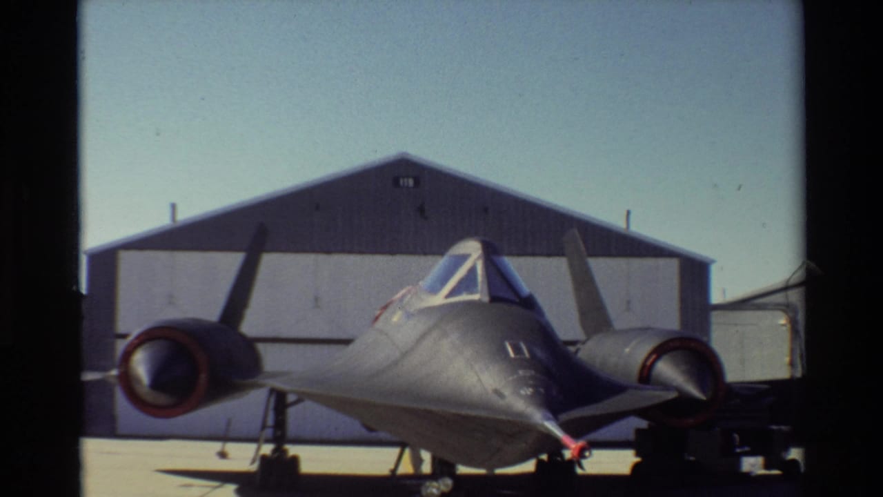 Front view of a black SR-71 aircraft parked on tarmac outside a hangar.