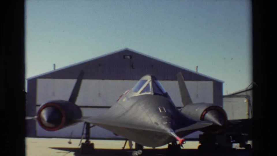 1981 Beale AFB frame showing a front view of the SR-71 Blackbird, with twin engine nacelles, landing gear, and a hangar in the background.