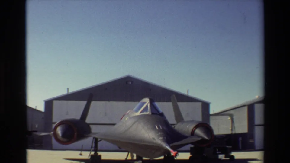 1981 Beale AFB 8mm frame showing the SR-71 Blackbird from the front, with its engines, canopy, landing gear, hangar, and open tarmac visible.