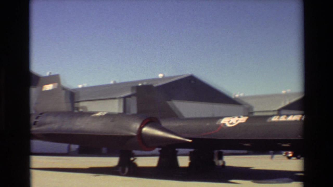 Rear and side section of a black SR-71 aircraft parked in front of hangars.