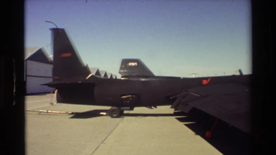 1981 Beale AFB home-movie frame showing the SR-71 tail, wing, landing gear, and hangars in the background.