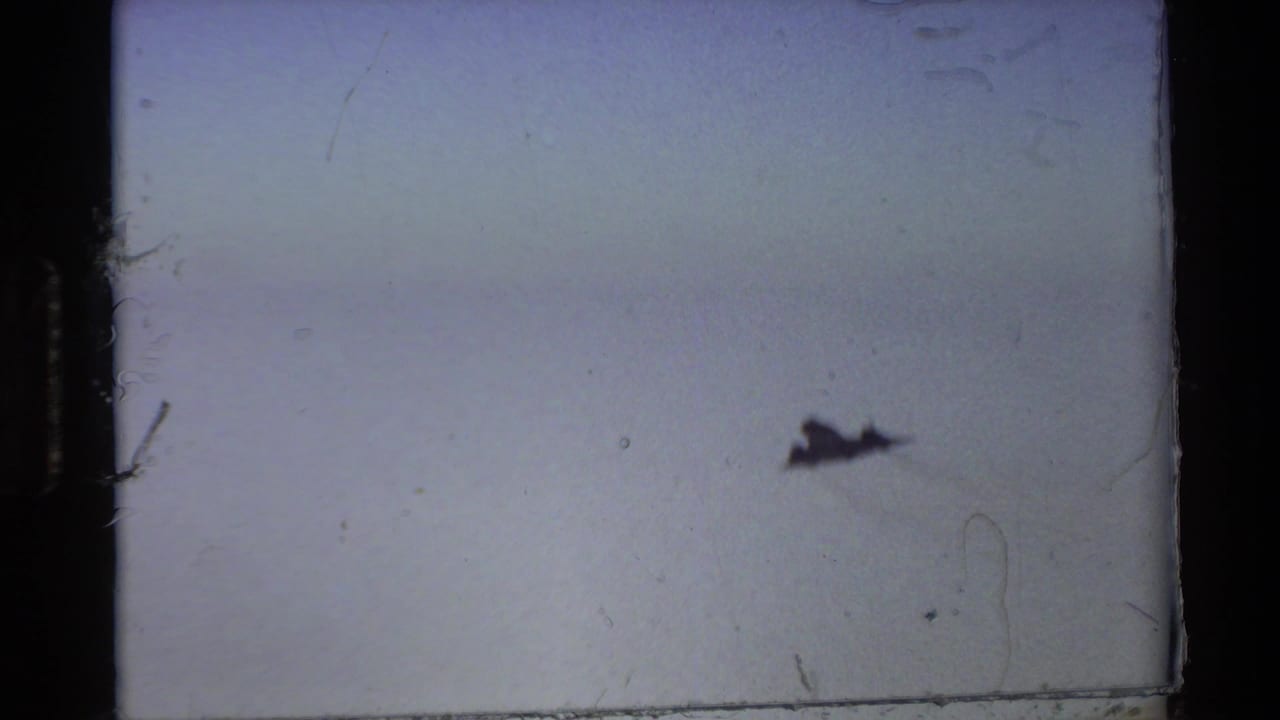 Small dark jet silhouette flying against a pale blue sky.