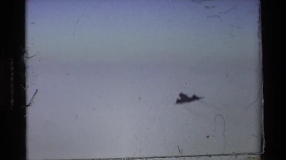 A distant black jet appears in flight against the clear sky in this 1981 Beale AFB 8mm frame.
