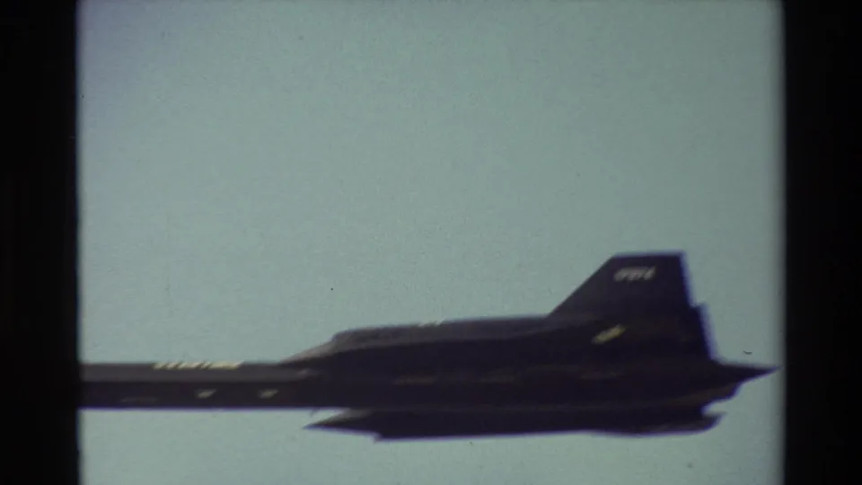 Close 8mm view of a dark military jet passing over Beale AFB, with tail markings indistinct and film borders visible.