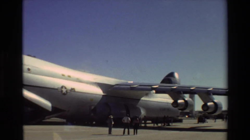 Wide 1981 Beale AFB home-movie frame showing a large white U.S. Air Force aircraft, open ramp, engines, and people on the tarmac.