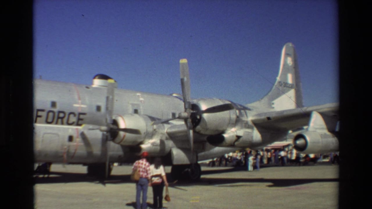 1981 Beale AFB home-movie frame showing visitors near a silver Air Force propeller aircraft on a sunny tarmac.