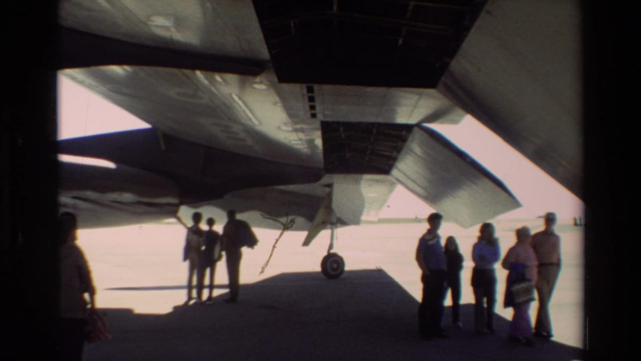 Underwing view at Beale AFB shows visitors and personnel standing in shadow beneath the B-52, with landing gear and aircraft structure visible.