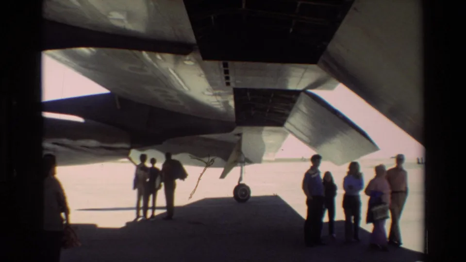 Underwing view at Beale AFB shows visitors and personnel standing in shadow beneath the B-52, with landing gear and aircraft structure visible.