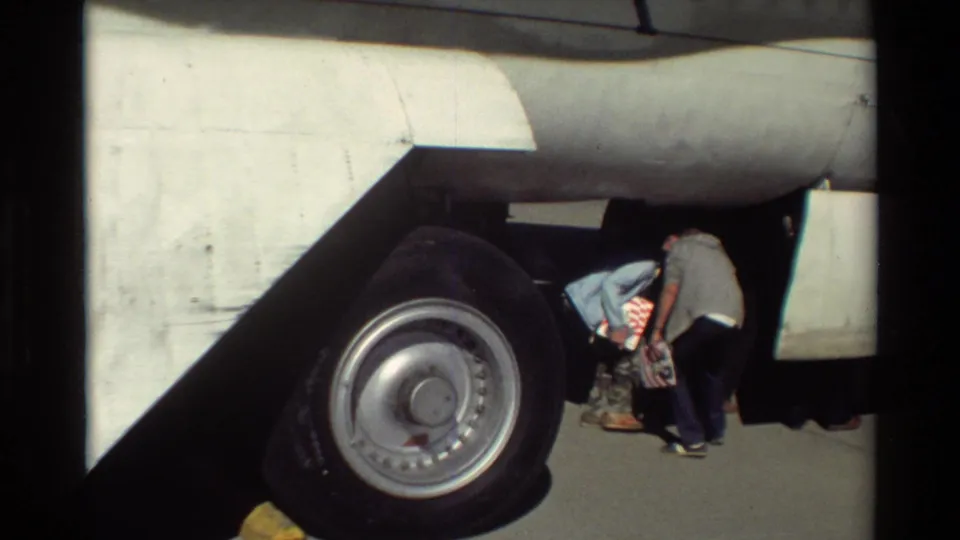 Close 8mm view of the B-52 landing gear at Beale AFB, with two visitors bending near the large wheel and underside of the aircraft.