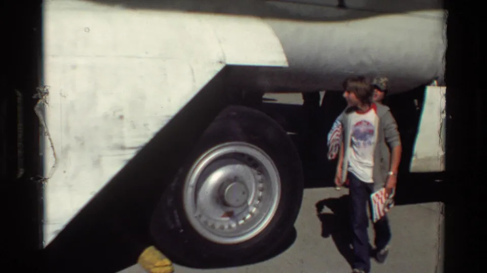 Beale AFB home-movie frame shows a man walking past the B-52 landing gear, with the large wheel and aircraft underside filling the background.