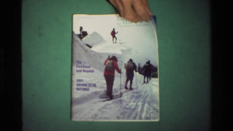 A hand enters at the top edge and holds the Sierra cover, suggesting the magazine is being turned on the green surface.