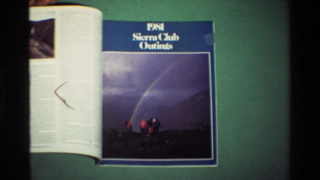 1981 Sierra Club Outings magazine lies open on a green surface, with a blue cover and small hikers under a rainbow in the printed photo.