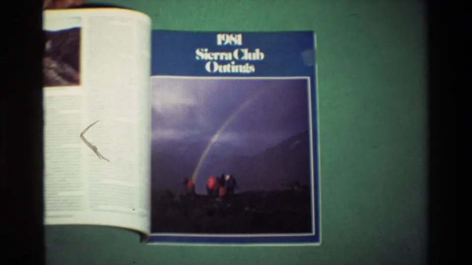 1981 Sierra Club Outings magazine lies open on a green surface, with a blue cover and small hikers under a rainbow in the printed photo.