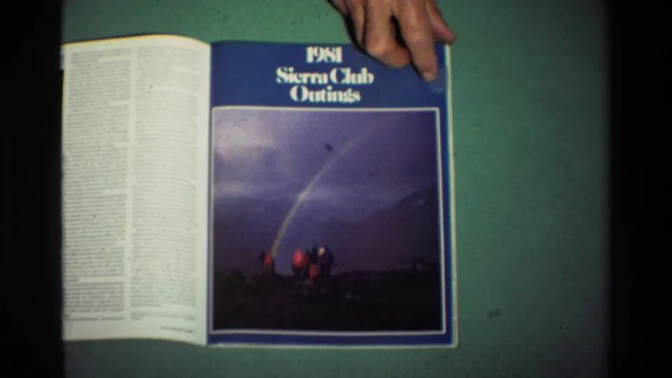 A hand rests on the open 1981 Sierra Club Outings magazine as the cover page with rainbow and hikers remains visible.