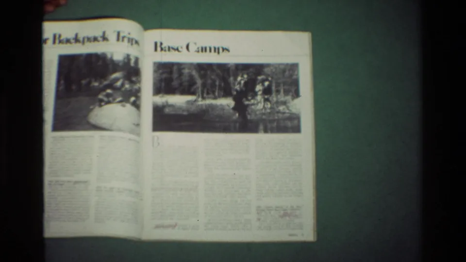 The magazine is open to interior pages with backpack trip and base camp headings, printed outdoor photographs, columns of text, and a hand at the edge.