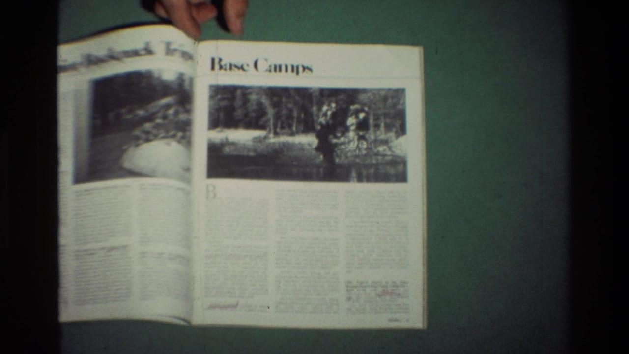 A hand holds open a magazine showing outdoor articles and black-and-white recreation photos, from archival 8mm footage dated 1981 in the metadata.