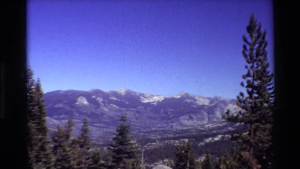 The 8mm home-movie view holds on a mountain range and valley, with tall evergreens silhouetted against the brightening sky.