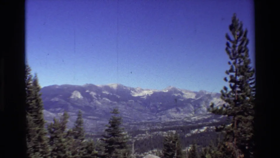 By the final frame, daylight shows a blue sky, snowy mountain ridge, forested valley, and evergreen trees along the overlook.