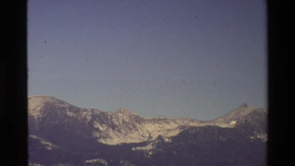 Tight 8mm view of rugged mountain peaks and snow patches beneath a clear sky, with soft focus and visible film grain.
