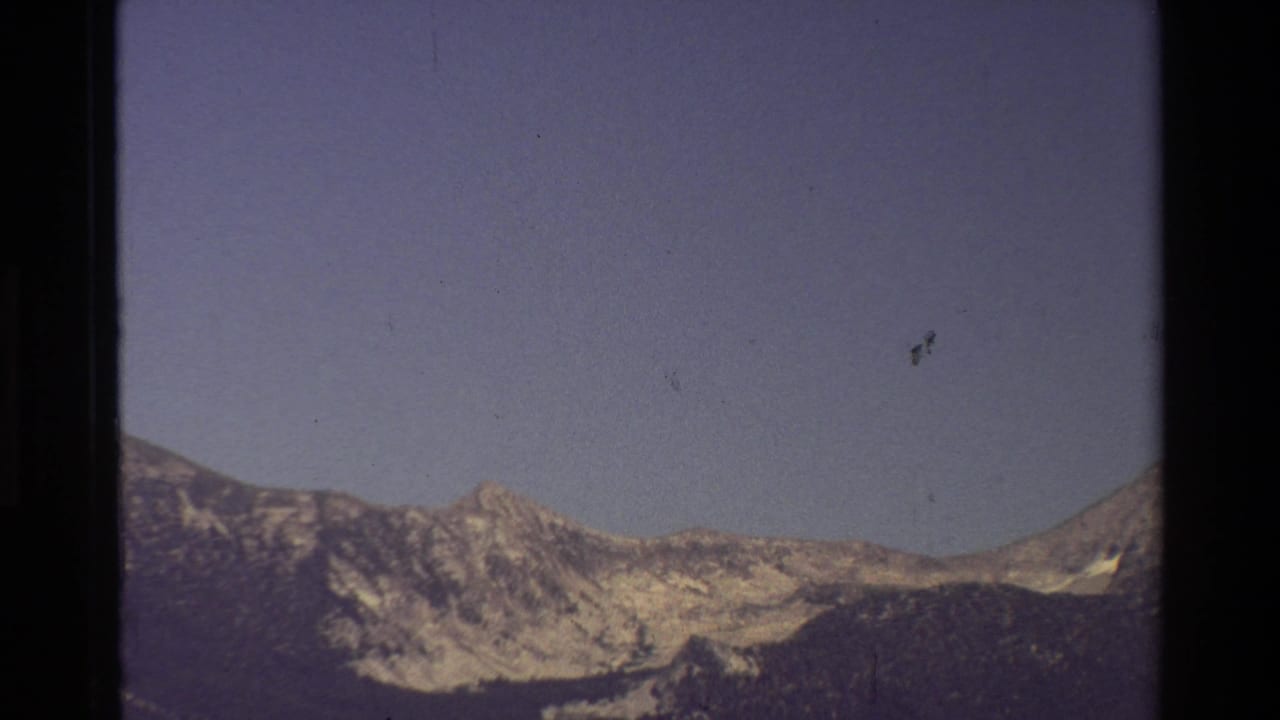 1981 8mm frame of a distant mountain ridge under a dark blue-purple sky, with visible film borders and dust marks.
