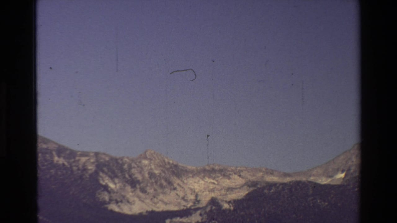 1981 8mm view of a mountain ridge under muted sky, with dark film borders and visible surface marks.