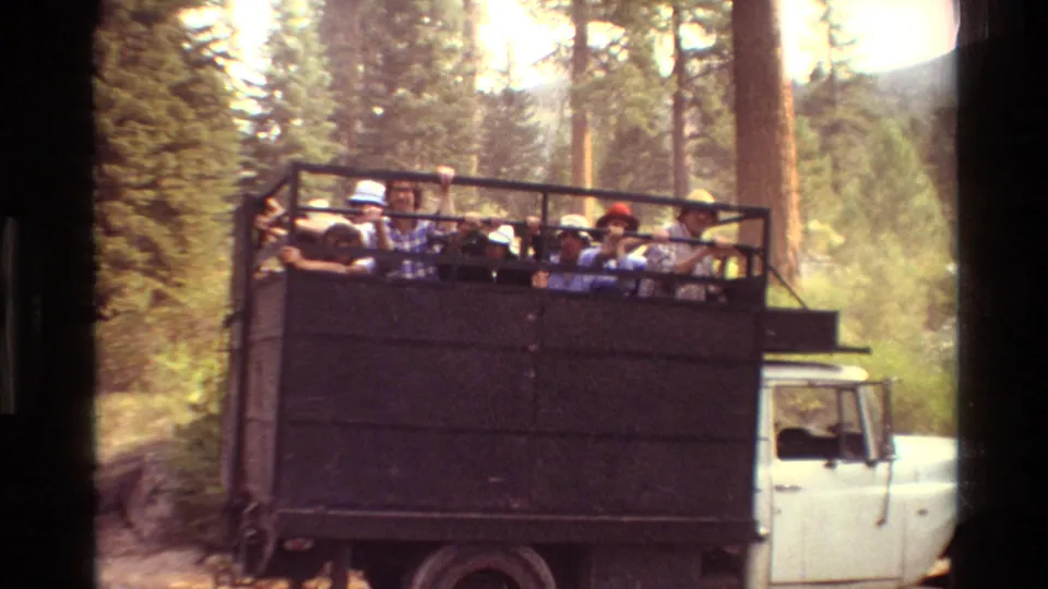 A closer 8mm frame shows several visible faces in an open truck on a forested mountain road, with the white cab at right.