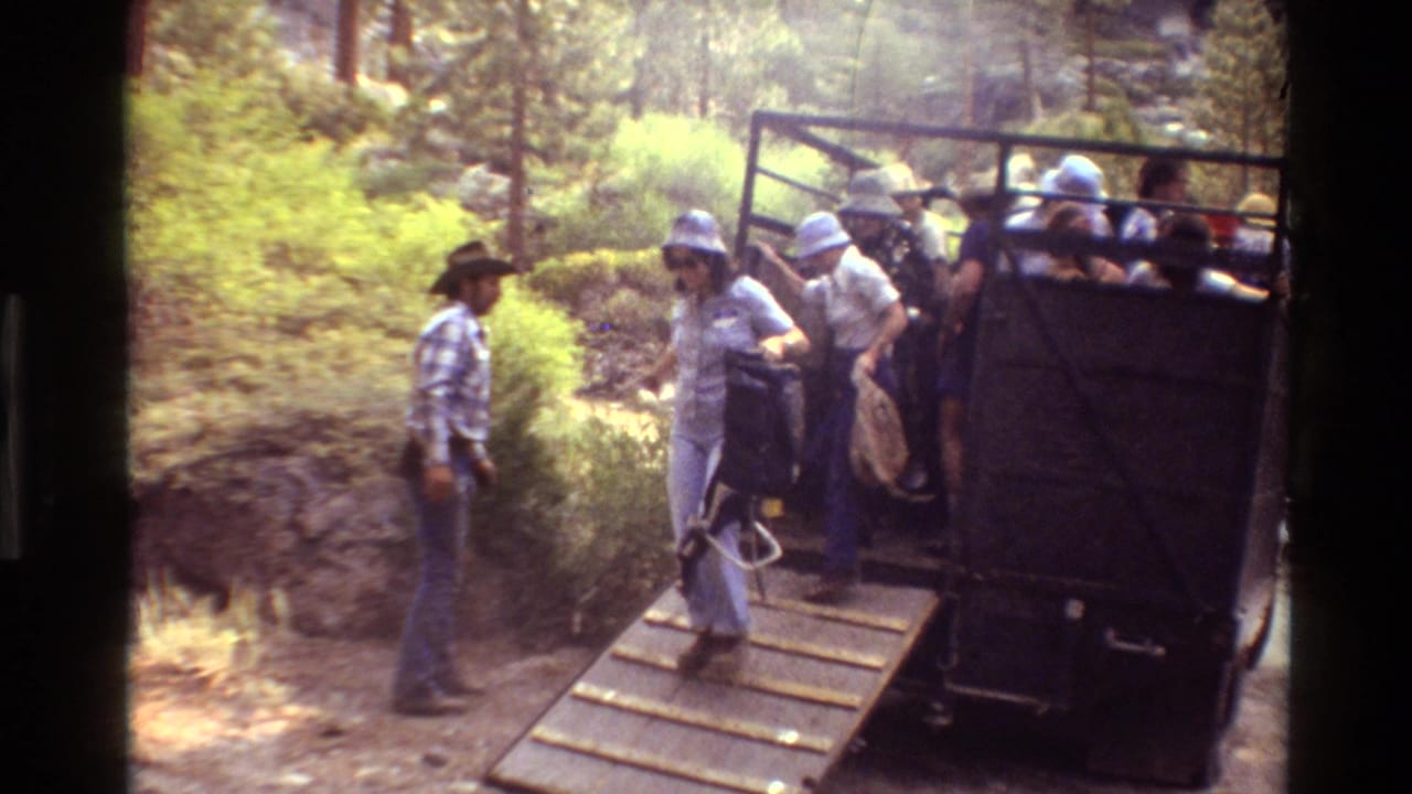 1981 home-movie frame of hikers in hats and casual outdoor clothing boarding an open utility truck in a wooded mountain area.