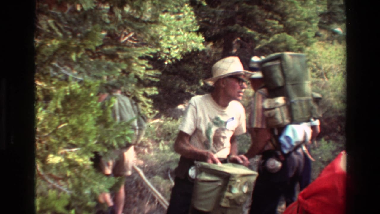 1981 8mm frame of hikers in a wooded area, including a man in a brimmed hat and others carrying large packs.